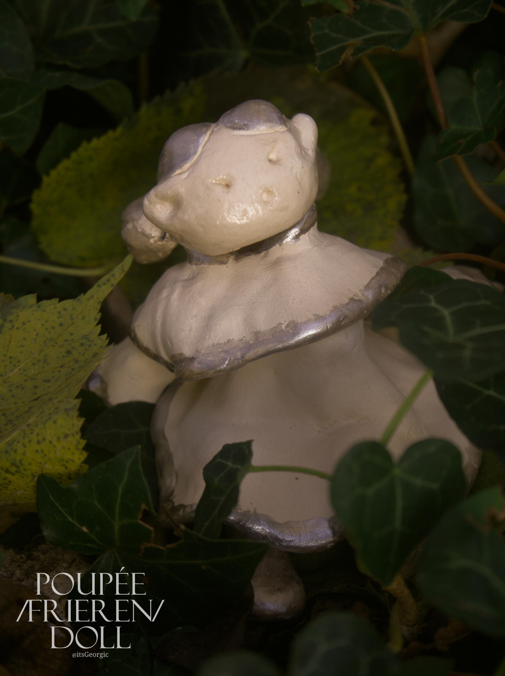 Photo de la poupée Frieren vue de 3/4 en contre plongée dans un parterre de lierre et de feuilles