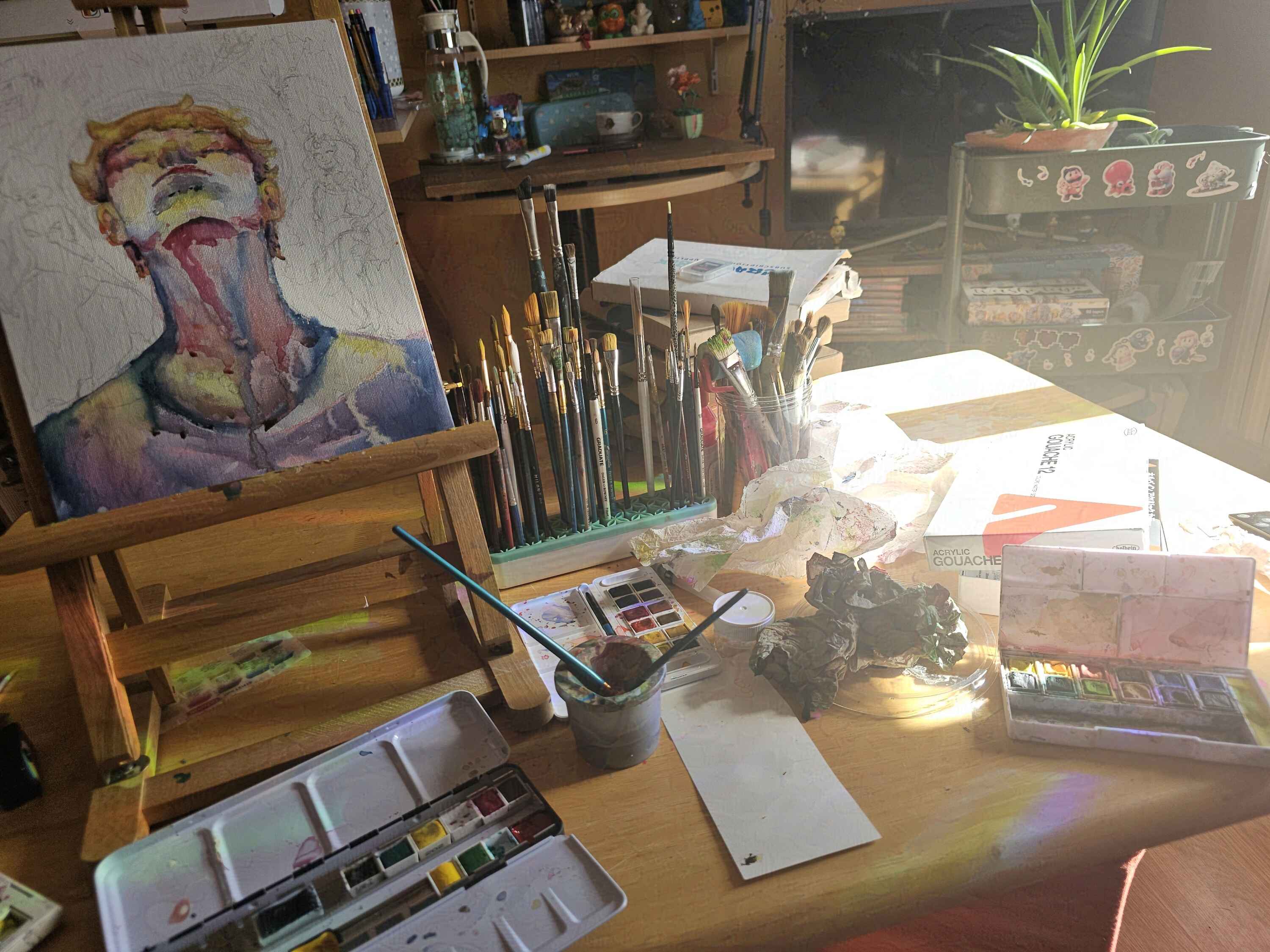 Photo de la toile en cours de création, il y a juste le portrait à l’aquarelle qui est fait. La toile est posée sur une table couverte de peinture et pinceaux dans un atelier.